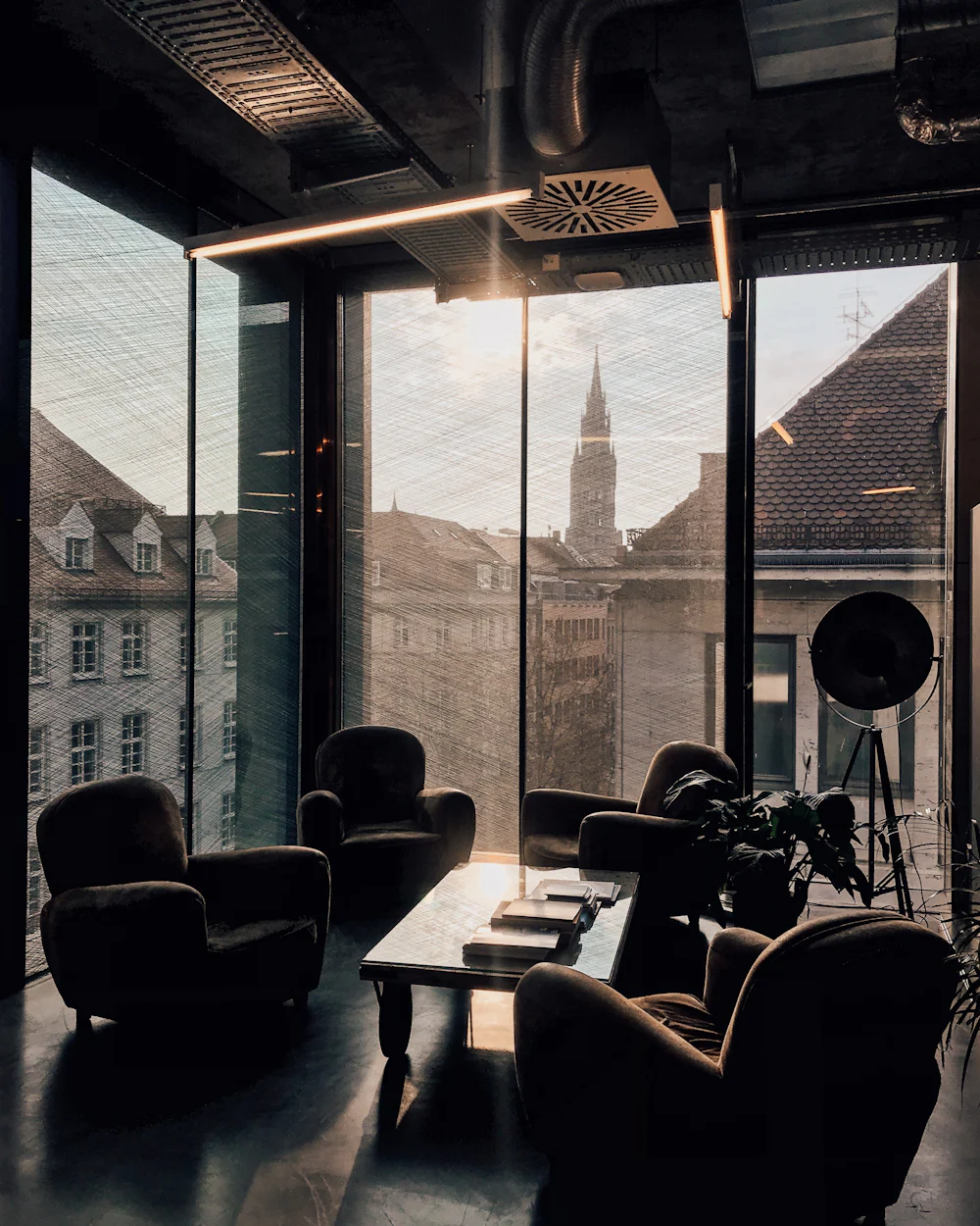 A quiet coworking lounge at golden hour, with armchairs facing tall windows above the rooftops.
